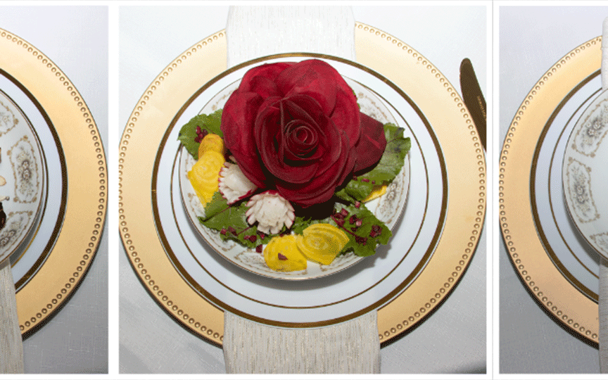 A trio of ornate, gold-rimmed plates set on a white tablecloth. Each plate is centered with a vibrant red rose atop colorful vegetables, exuding elegance.