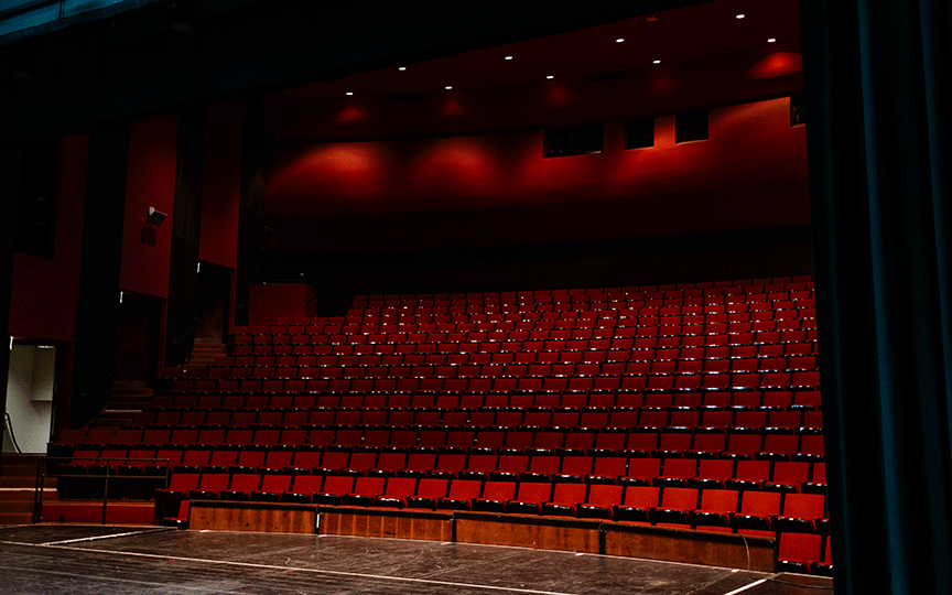 Mary Jane Teall Theater empty with rows of red seats under dim lighting. The stage is partially visible, conveying a quiet, anticipatory atmosphere.